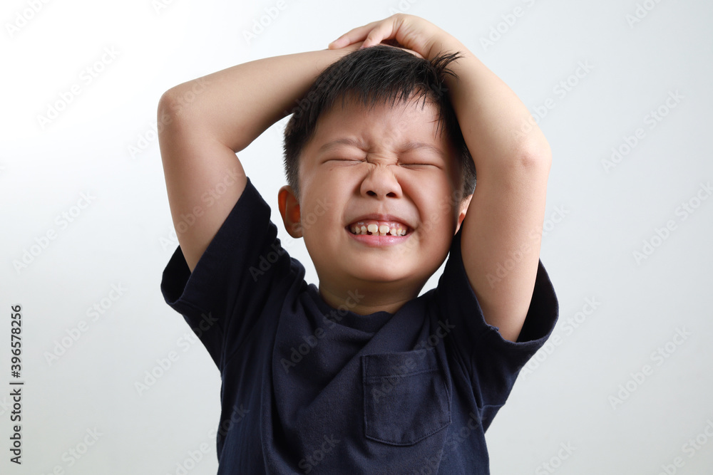 A frustrated Asian boy holding his head, standing against a light background. A frustrated Asian boy holding his head, standing against a light background.