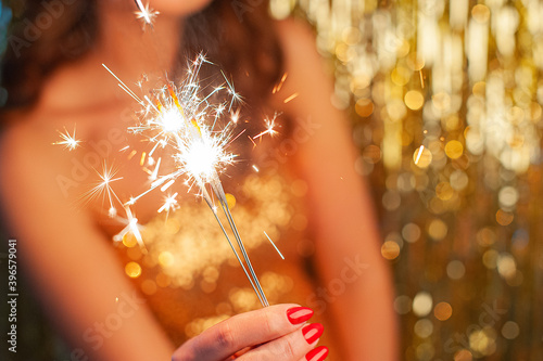 Portrait of a woman in a gold dress holding a sparkler on a bright gold background, selective focus