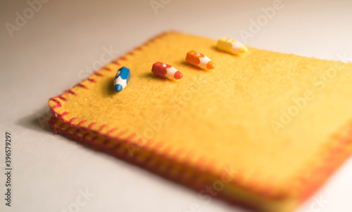 Handmade yellow-orange pin cushion with buttons in the form of colored pencils. Edged with red thread. Lies on a white background