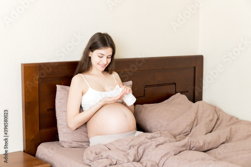 pregnant woman applying stretch mark cream to belly. pregnancy, people and maternity concept. pregnant apply anti-stretch mark cream on her belly