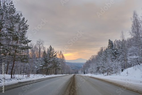 Winter road leading to the mountain through the forest at dawn
