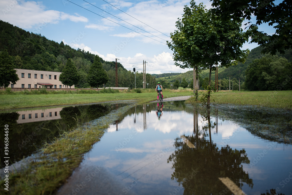 Fototapeta premium Young athlete woman riding a bicycle on a road through the water.