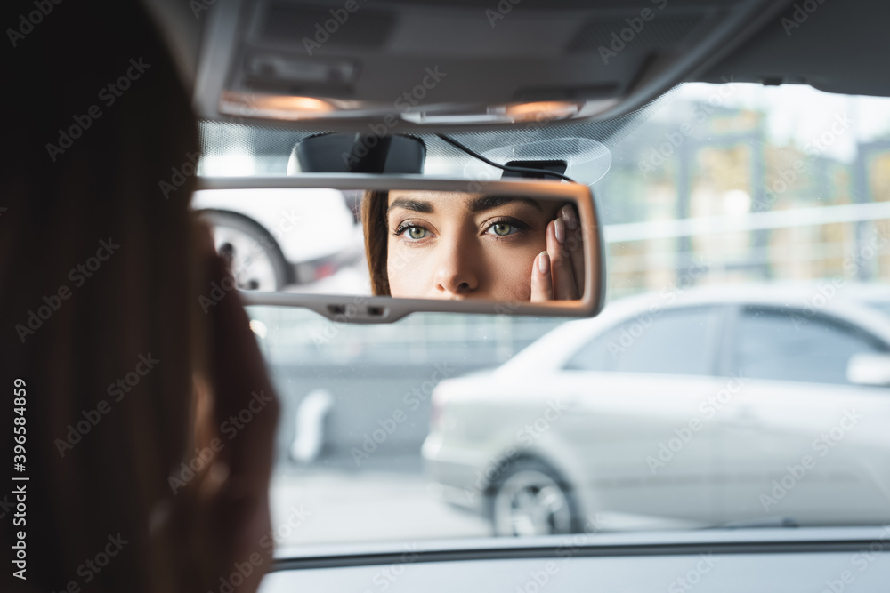 woman in car touching face while looking in rearview mirror on blurred woman in car touching face while looking in rearview mirror on blurred