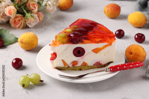 Slice of delicious jelly cake with fruits and berries on a plate on a gray background. Closeup. Horizontal format