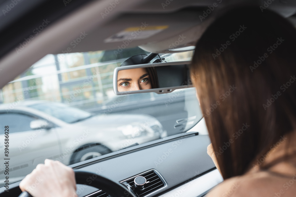 woman driving car and looking in rearview mirror on blurred  - obrazy, fototapety, plakaty 