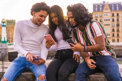 Lifestyle, three black friends having fun and watching social media on the street. Afro hair boy, brunette boy with long hair and brunette girl