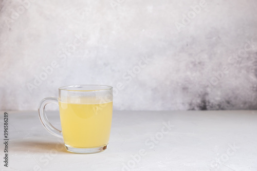 Delicious homemade chicken broth in a glass cup on a light gray background.