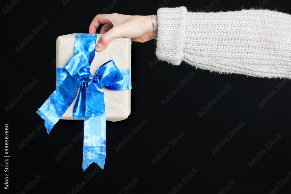 The girl is holding a gift with a blue bow in her hands. Gift in craft paper. Beautiful blue bow. A Christmas gift. New Year. Gift on black background The girl is holding a gift with a blue bow in her hands. Gift in craft paper. Beautiful blue bow. A Christmas gift. New Year. Gift on black background