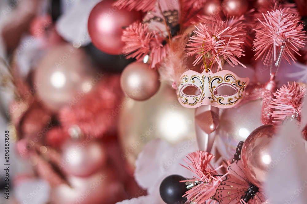 Christmas toy on a pink Christmas tree in the form of a beautiful masquerade mask against the background of other Christmas balls decorating the Christmas tree