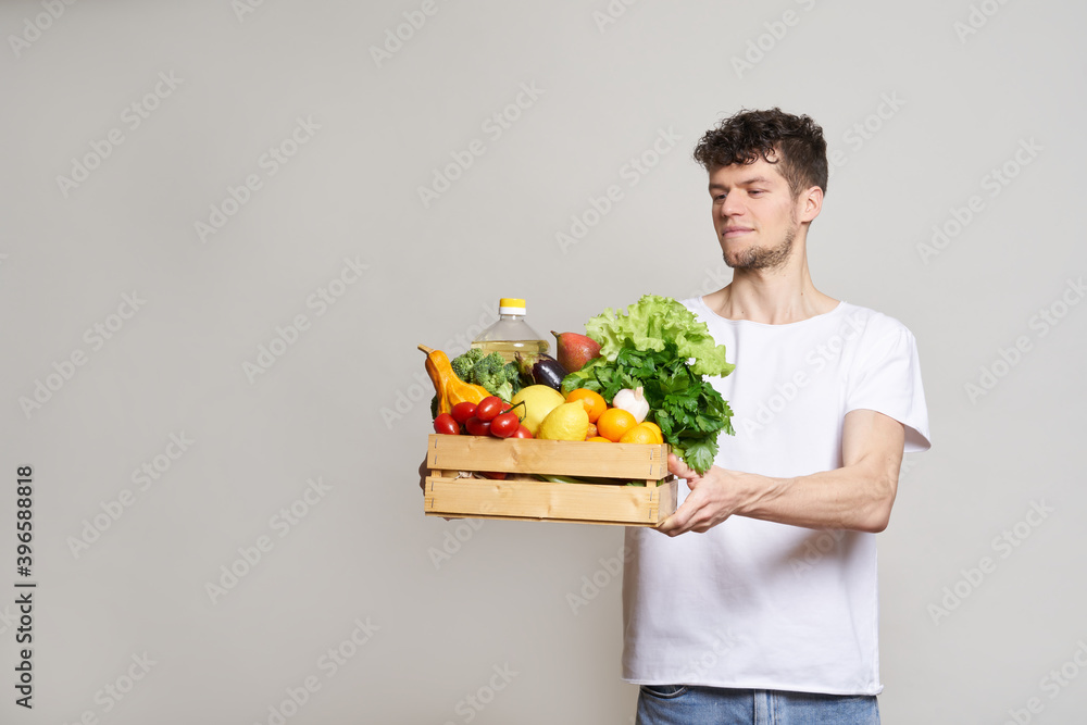 online shopping concept. A man in T-shirt holds a box of fresh food in his hands. Food delivery from the supermarket, from farmers. Delivery during quarantine online shopping concept. A man in T-shirt holds a box of fresh food in his hands. Food delivery from the supermarket, from farmers. Delivery during quarantine
