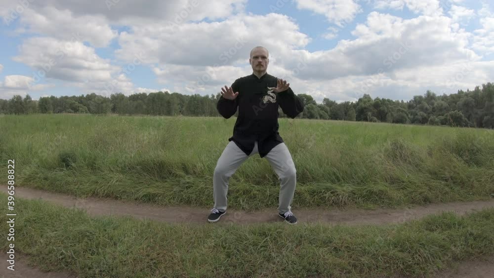 European man in Chinese clothes is engaged in qigong gymnastics in a Park. The person makes slow, smooth movements European man in Chinese clothes is engaged in qigong gymnastics in a Park. The person makes slow, smooth movements