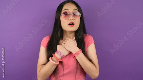 close-up portrait of young suddenly frightened hipster asian woman on isolated purple background. A woman in fashionable violet glasses. 4K