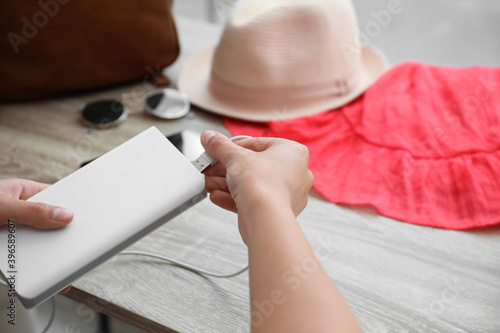 Woman charging mobile phone with power bank while getting ready for travel, closeup