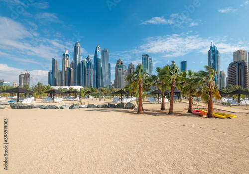 Fototapeta Naklejka Na Ścianę i Meble -  Sandy beach with  coconut palm trees against the background of Dubai Marina skyscrapers