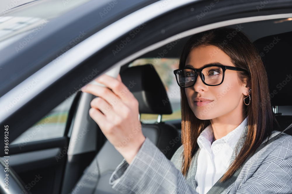  businesswoman in eyeglasses sitting in car on blurred foreground