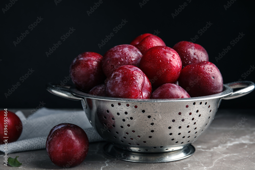 Delicious ripe plums in colander on grey marble table Delicious ripe plums in colander on grey marble table