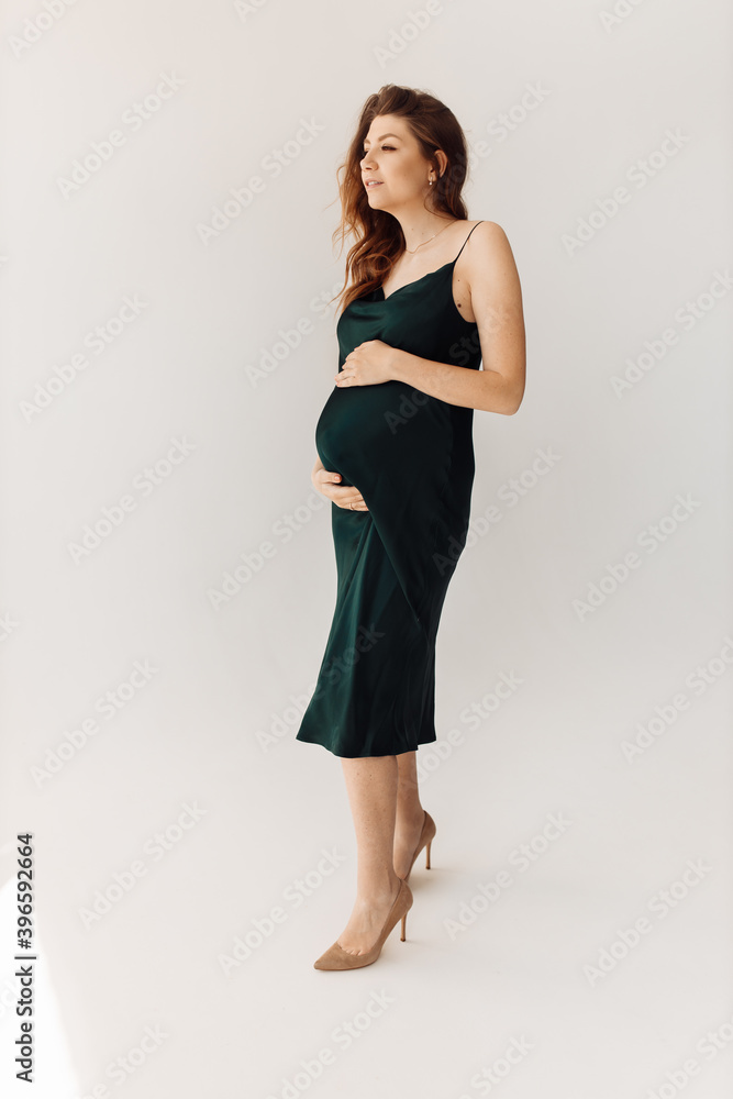 Wonderful pregnant woman stand in studio, posing, wearing green dress, expect for a first baby, happy lady excited about maternity, enjoy pregnancy, motherhood concept Wonderful pregnant woman stand in studio, posing, wearing green dress, expect for a first baby, happy lady excited about maternity, enjoy pregnancy, motherhood concept