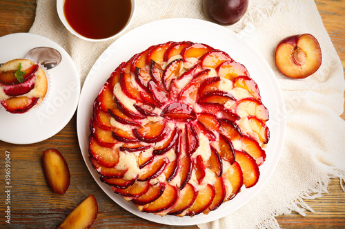 Delicious cake with plums on wooden table, flat lay