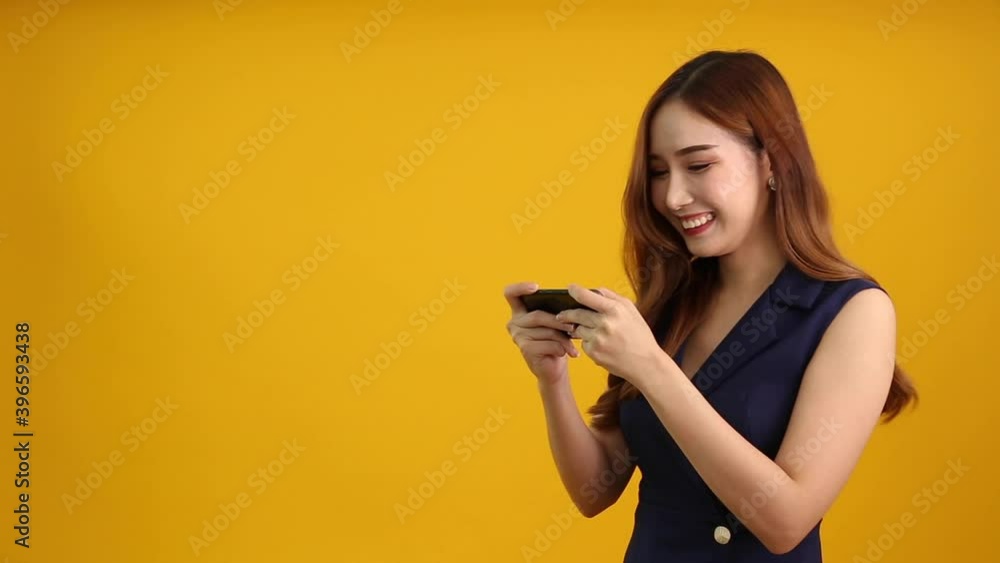 Asian woman gamers play online games on smartphone isolated on yellow background, Entertained with awesome application concept Asian woman gamers play online games on smartphone isolated on yellow background, Entertained with awesome application concept