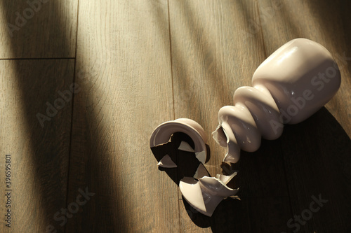 Broken pink ceramic vase on wooden floor. Space for text photo