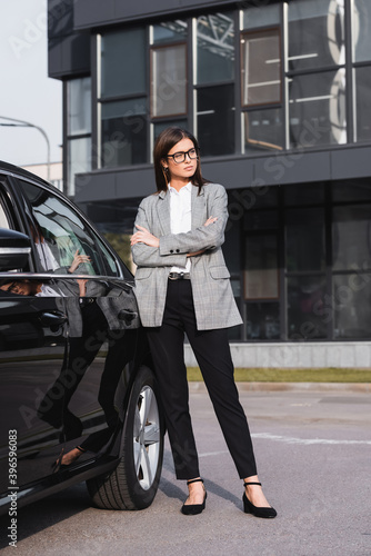  confident businesswoman standing near black car with crossed arms
