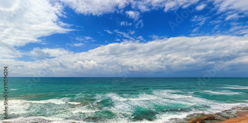Fototapeta Naklejka Na Ścianę i Meble -  Magnificent sea panoramic landscape. White foaming waves surf. Stony seashore. Seascape with impressive blue sky and white bizarre clouds