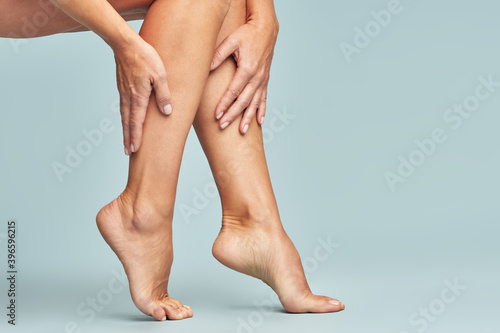 Cropped shot of a woman touching her legs with smooth, silky and soft skin after making a depilation, sitting over blue background photo