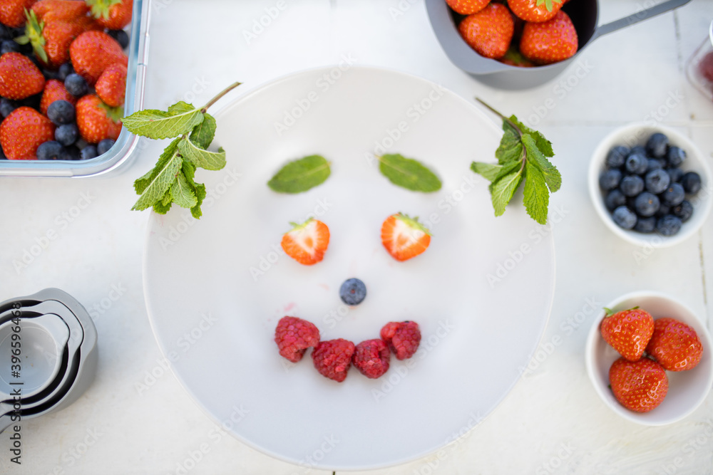 Smiling face made with berries and mint leaves on a plate Smiling face made with berries and mint leaves on a plate