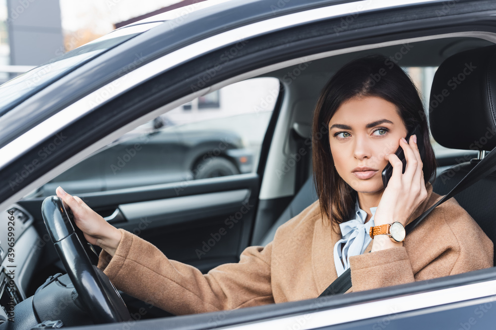  woman in trench coat talking on smartphone while driving car