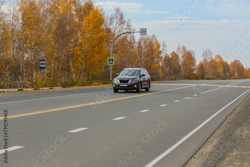 Car moves along a suburban highway along autumn forest