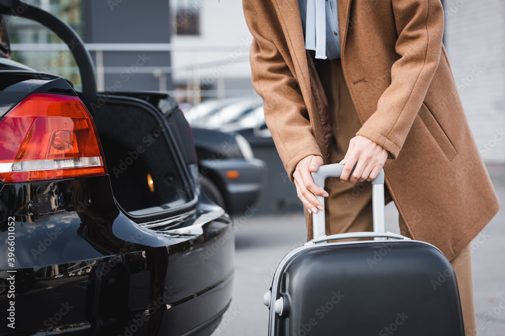 partial of woman in autumn clothes holding suitcase near open car trunk partial of woman in autumn clothes holding suitcase near open car trunk