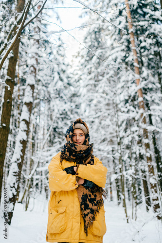 Young stylish hipster girl in yellow jacket covering the head with a warm scarf and posing in the forest