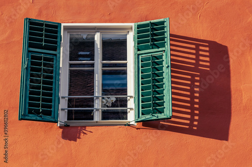 window with open shutter and flower in an old house in the countryside, shadow on the wall