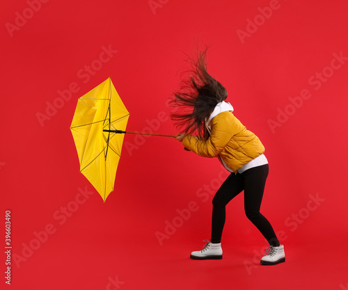 Woman with umbrella caught in gust of wind on red background