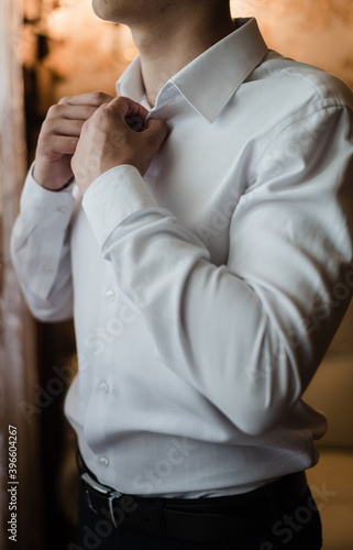 man in white shirt, the groom buttons his shirt