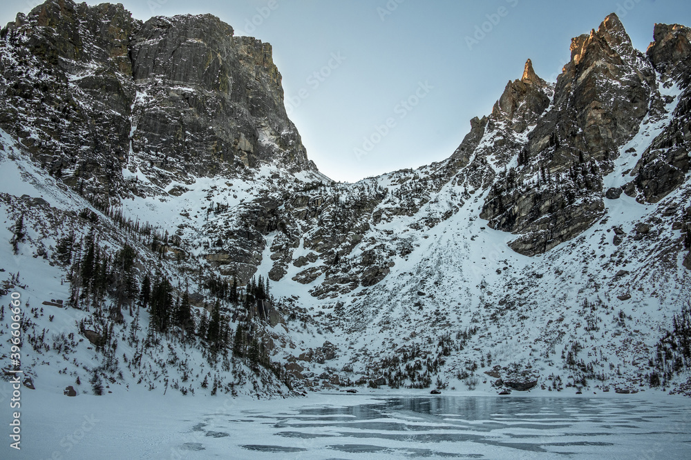 View of Emerald Lake in Rocky Mountain National Park in Colorado during the winter. The lake is frozen over and the mountain range is covered in snow.