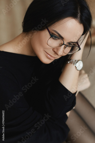 Close portrait of a young model woman with perfect face skin and gentle makeup in round glasses looking down