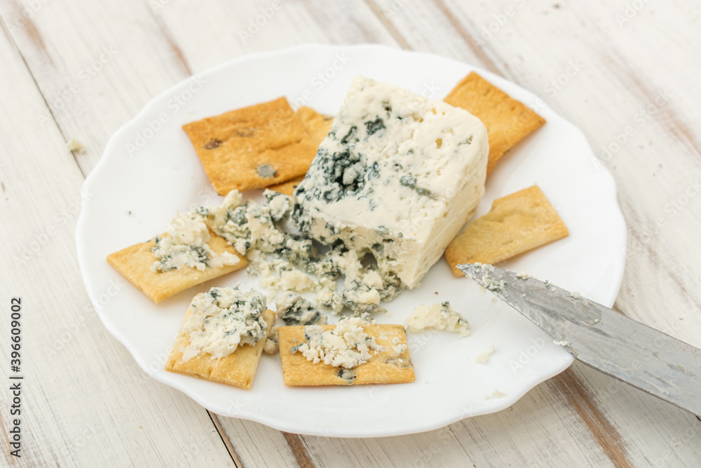 Blue cheese and cracker on a white plate on a wooden background.
