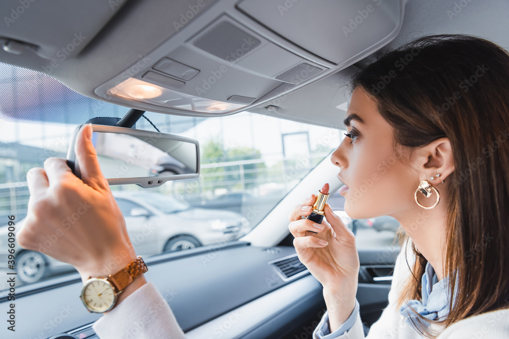  woman holding lipstick while looking in car rearview mirror