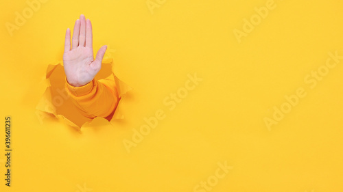 Woman hand arm showing stop gesture with palm isolated through torn yellow wall background studio. Copy space advertisement place for text mage promotional content. Advertising area workspace mock up. photo