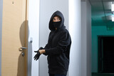 Thief broke into the apartment. House robbery by woman in a black jacket and black mask black gun and crowbar. Burglar in a mask. Thief in a mask trying to break into other people's house.