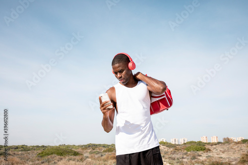 Young black sportsman with headphones who operates the mobile. Concept of sport.