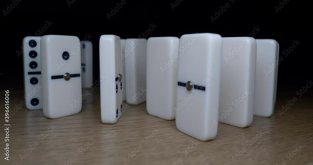 Close up of white dominoes falling down on wooden background. Selective focus. The last tile doesn’t fall. Concept of domino effect, chain reaction, risk management. Close up of white dominoes falling down on wooden background. Selective focus. The last tile doesn’t fall. Concept of domino effect, chain reaction, risk management.