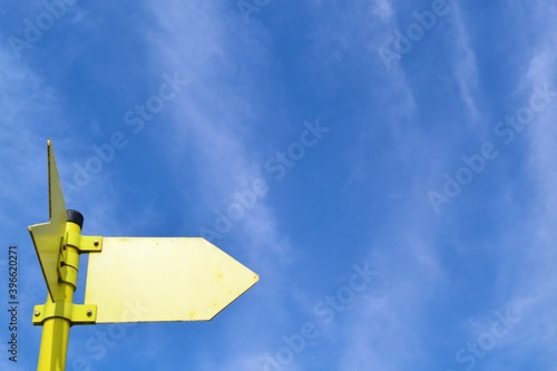 Metallic yellow arrow on blue sky background with white clouds