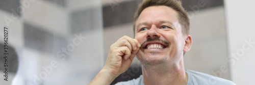 Man smiles and holds his mustache in front of mirror. How to shave your mustache concept