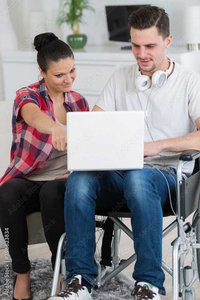 Fototapeta premium man with laptop on wheelchair with woman showing her something