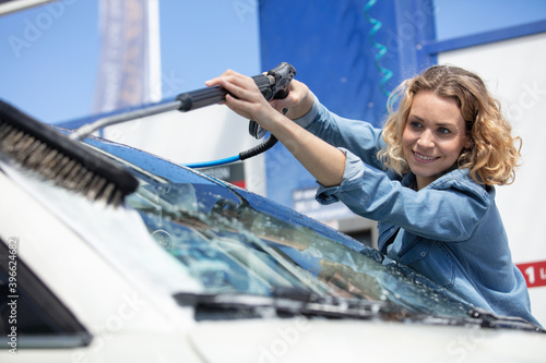 positive woman washing windshield of car