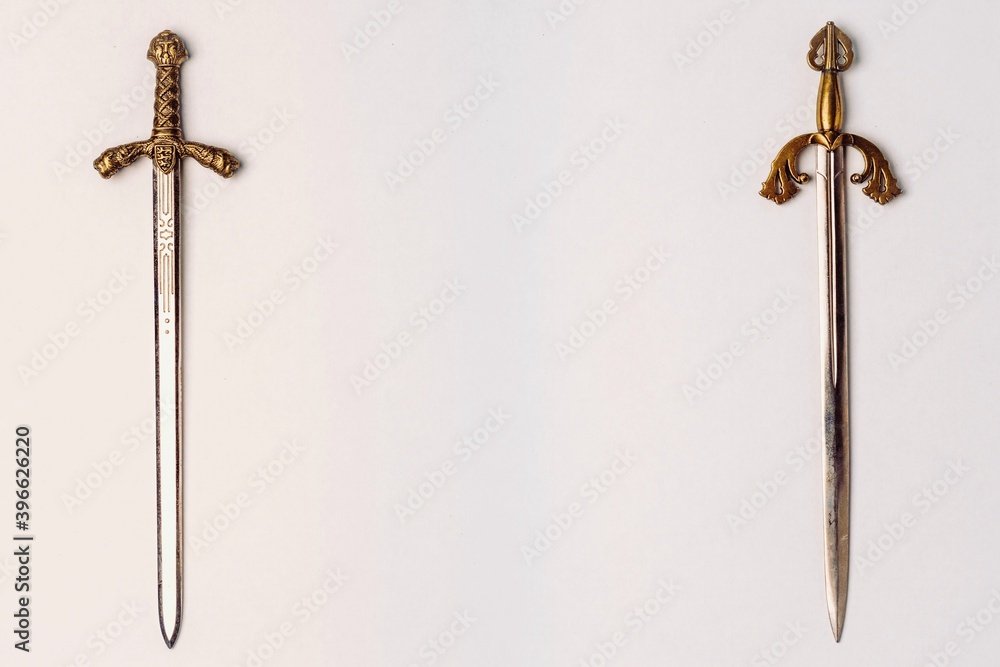 Two ancient knightly swords with golden hilts with engraving isolated on a white background. Horizontal position, copy space Two ancient knightly swords with golden hilts with engraving isolated on a white background. Horizontal position, copy space