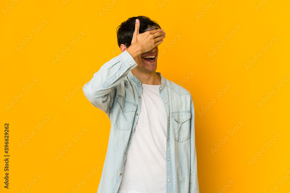 Young skinny hispanic man covers eyes with hands, smiles broadly waiting for a surprise. Young skinny hispanic man covers eyes with hands, smiles broadly waiting for a surprise.