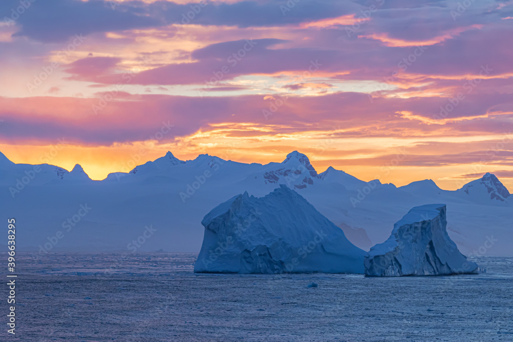 Insanely beautiful iceberg in the sunset light of the sun hiding behind the mountains in the background. Photo of an iceberg in the evening with little light